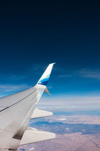 Airplane wing flying over landscape against blue sky