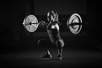 Woman lifting barbell in darkroom