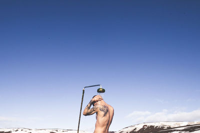 Rear view of man bathing against blue sky