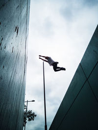 Low angle view of man flying over buildings against cloudy sky