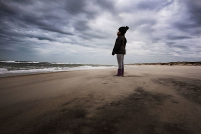Young girl watching the ocean under cloudy skies