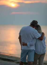 Rear view of mature couple looking at sea during sunset