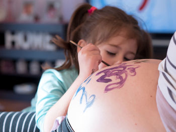 Girl painting pregnant mother belly at home