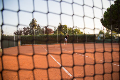 Man playing tennis on court seen through net