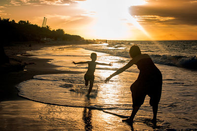 Silhouette men on beach against sky during sunset