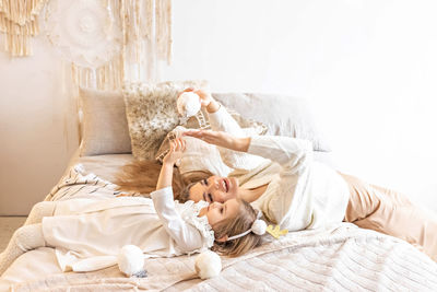 Mom and daughter play with fluffy soft snowballs, lying on the bed in a bright bedroom.family. ethno