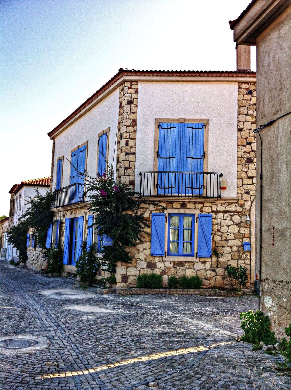 architecture, building exterior, built structure, blue, clear sky, street, window, house, residential building, residential structure, the way forward, building, sunlight, day, road, sky, cobblestone, outdoors, wall - building feature, no people