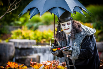 Portrait of man in costume smoking cigarette while holding umbrella