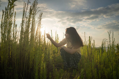 Side view of young woman on field against sky during sunset