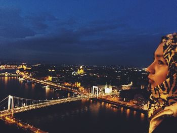 Illuminated bridge over river against sky in city at night