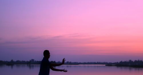 Silhouette man standing on pink lake against sky during sunset