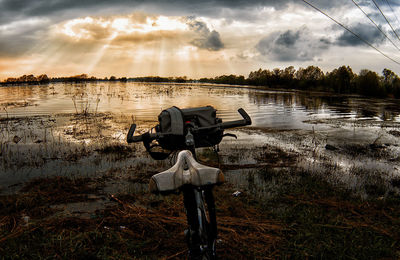 Man photographing by lake against sky during sunset