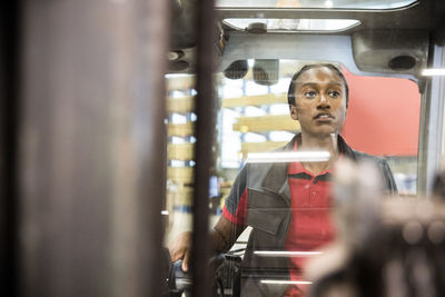 Female warehouse worker sitting in forklift while looking away at warehouse