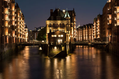 Bridge over river amidst buildings in city at night