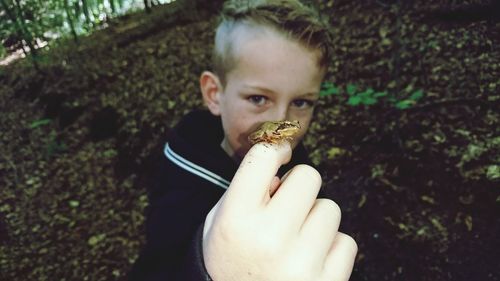 Portrait of boy showing frog sitting on finger