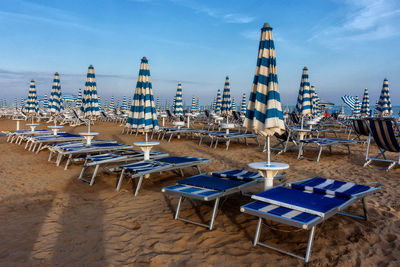 Empty chairs and tables on beach against blue sky