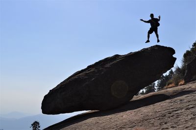 Low angle view of silhouette man jumping on rock against sky