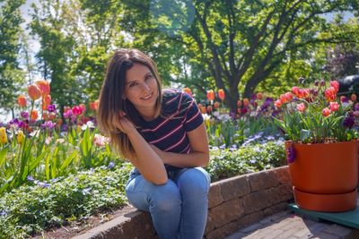 Portrait of smiling woman sitting against blooming tulips