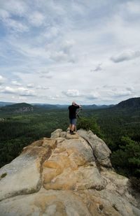 Rear view of man standing on rock formation against sky at hantzschelstiege