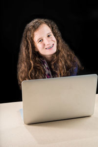 Portrait of young woman using laptop at desk against black background