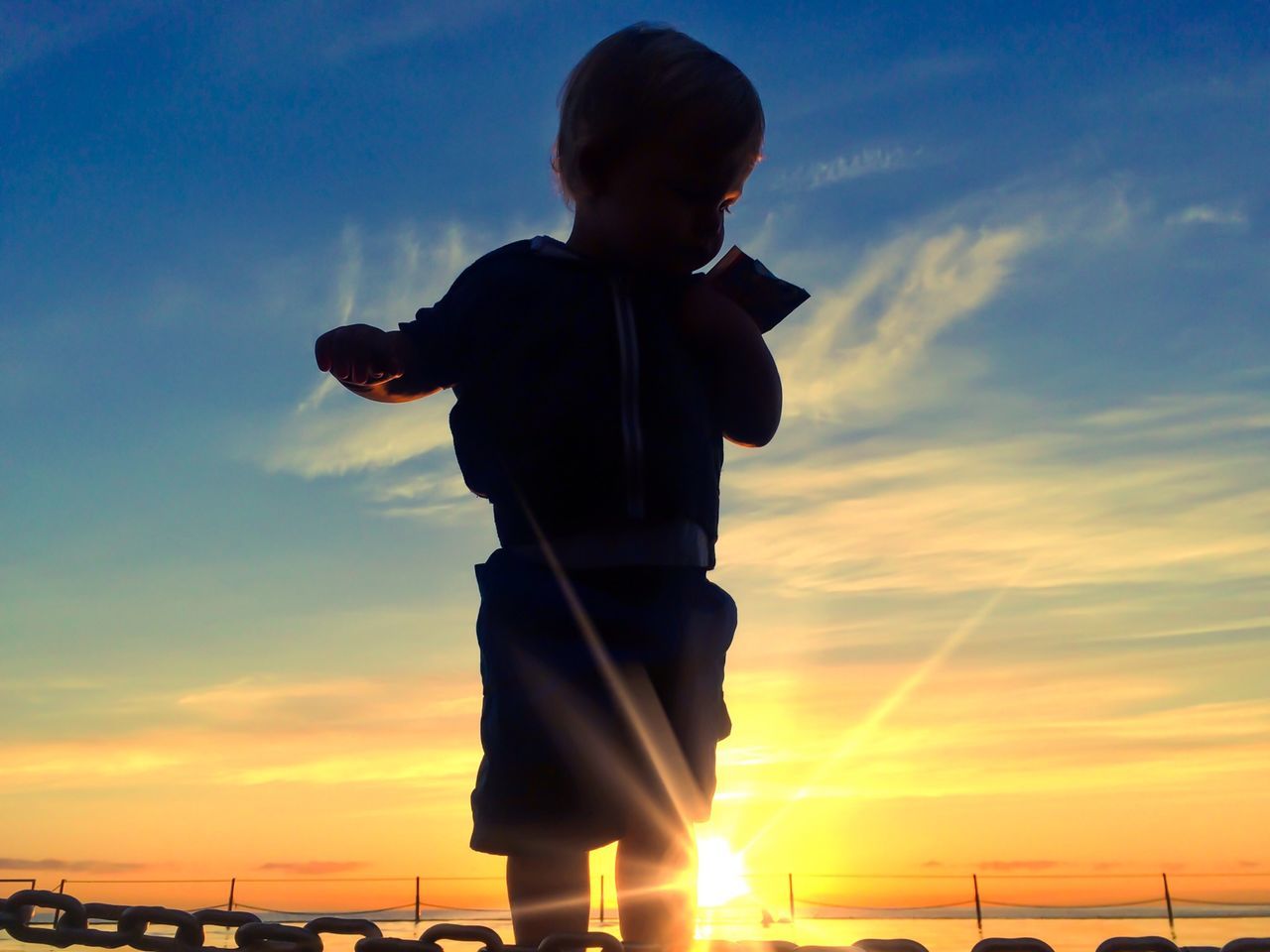 lifestyles, sunset, sky, standing, leisure activity, full length, casual clothing, cloud - sky, three quarter length, silhouette, low angle view, men, cloud, sun, sunlight, holding, side view, rear view