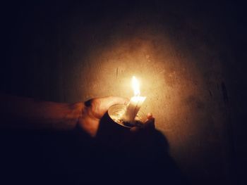 Close-up of hand holding lit candle in darkroom