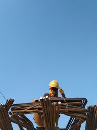 Low angle view of man working at construction site against clear blue sky