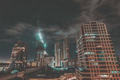 Illuminated modern buildings in city against sky at night