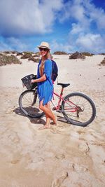 Full length of woman riding bicycle at beach against sky