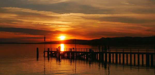 Silhouette wooden posts in sea against sky during sunset