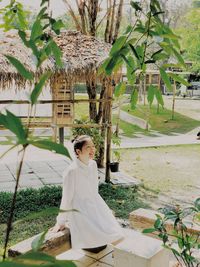 Young woman standing by palm tree against plants