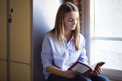 Schoolgirl reading book by window in locker room