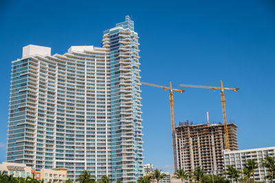 Low angle view of crane by building against clear blue sky