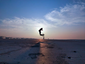 Silhouette man jumping at beach against sky during sunset