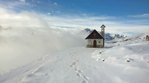 Chapel on snow covered field against sky