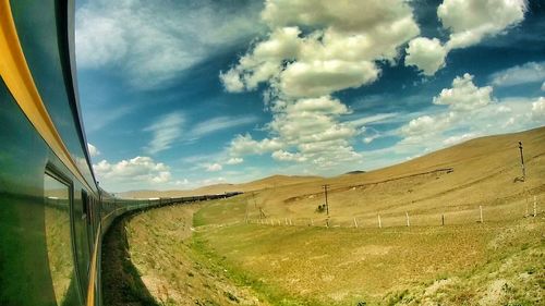 Road passing through field against cloudy sky