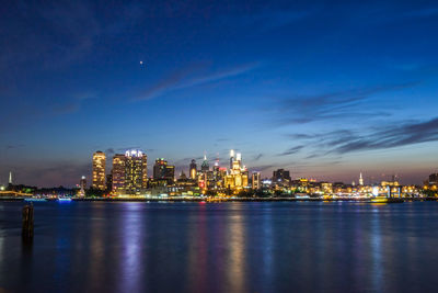 Illuminated city by river against sky at night