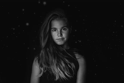 Portrait of girl with long hair standing against black background