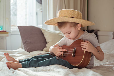 Cute boy playing ukulele at on bed