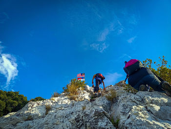 Low angle view of people on rock against blue sky