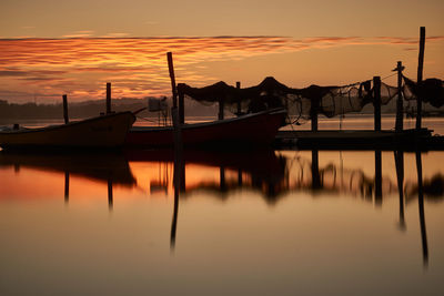 Wooden posts in lake against sky during sunset