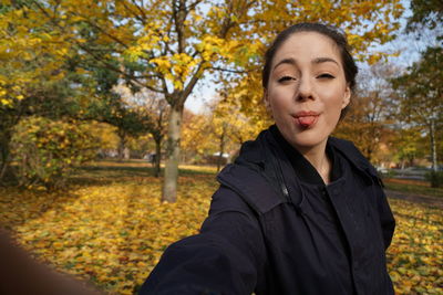 Portrait of smiling young woman standing at park during autumn