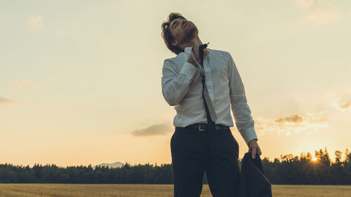 Man looking away on field against sky during sunset