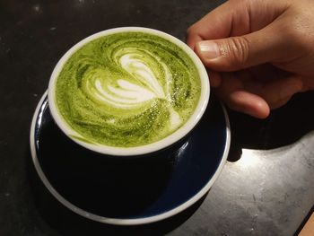 Human hand carries a cup of matcha latte with heart shaped foam decoration