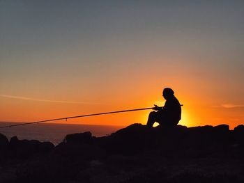 Silhouette man fishing at sea shore against sky during sunset