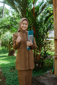 Portrait of young woman using mobile phone while standing against trees