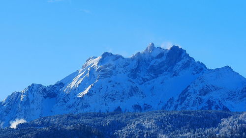 Low angle view of snowcapped mountains against clear blue sky