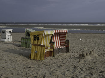 Hooded chairs on beach against sky