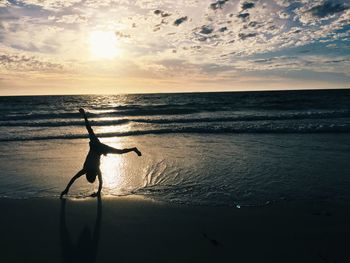 Silhouette man doing handstand at beach during sunset