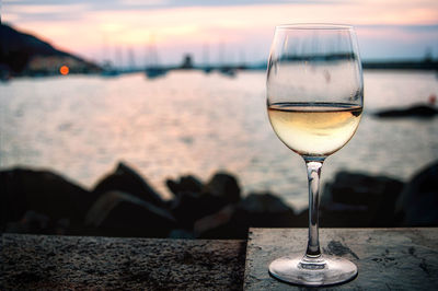 Close-up of wine in glass on table against sea during sunset